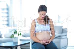 Pregnant woman looking at belly while sitting on chair
