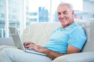 Portrait of happy senior man sitting on sofa with laptop