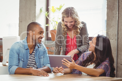 Smiling business people discussing over tablet in office