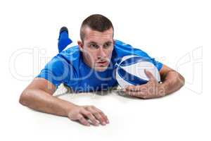 Rugby player looking away while lying in front with ball