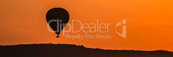 Balloon flying over horizon in orange sky