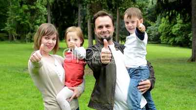 family (middle couple in love, cute girl and small boy) show thumbs on agreement in the park