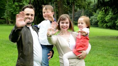 family (middle couple in love, cute girl and small boy) together waving hands in the park