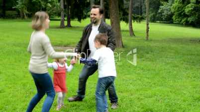 family (middle couple in love, cute girl and small boy) dance in circle in the park