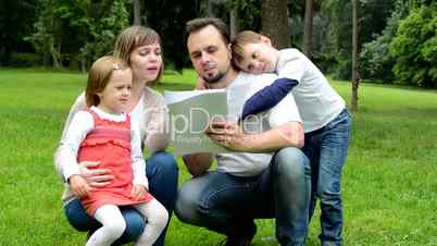 family (middle couple in love, cute girl and small boy) read document in the park