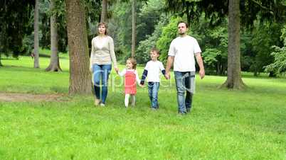 family (middle couple in love, cute girl and small boy) walking in park from distance to camera (beside camera)