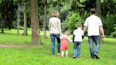 family (middle couple in love, cute girl and small boy) walking in park from camera (beside camera) to distance
