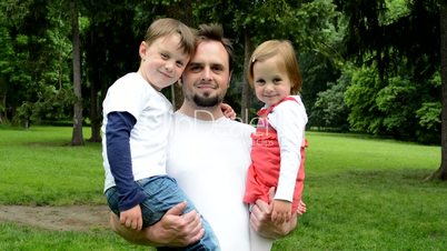 family (dad, little boy and cute girl) smile to camera - park