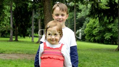 children (siblings - little boy and cute girl) smile to camera - park