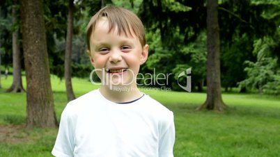 little cute boy laughs to camera - park in background - park
