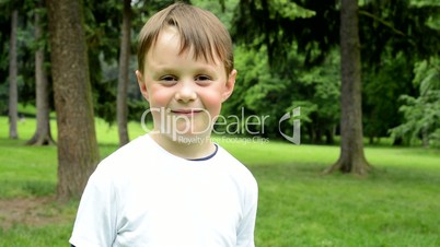 little cute boy smiles to camera - park in background - park