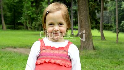 little cute girl smiles to camera - park in background - park