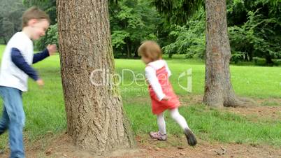 children (siblings - little boy and cute girl) playing in the park (running around trees)