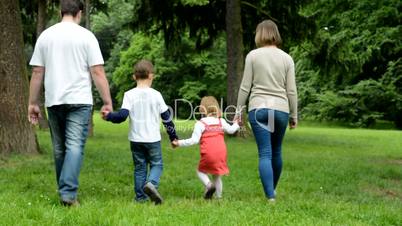 family (middle couple in love, cute girl and small boy) walking in park from camera to distance