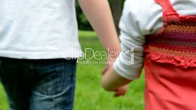children (siblings - boy and girl) holding hands and walking in park