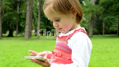 young little girl works on smartphone - park