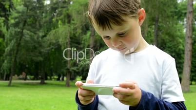 young little boy works on smartphone - park