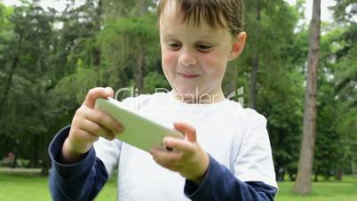 young little boy plays games on smartphone - park