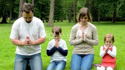 family (middle aged couple in love, boy and girl) pray in park (family kneeling on knees)