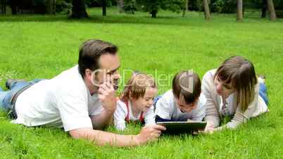 family (middle aged couple in love, boy and girl) lying in grass and work on tablet