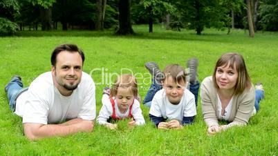 family (middle aged couple in love, boy and girl) lying in grass and smile to camera
