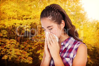 Composite image of sick woman sneezing in a tissue