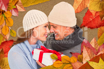 Composite image of casual couple in warm clothing holding gift