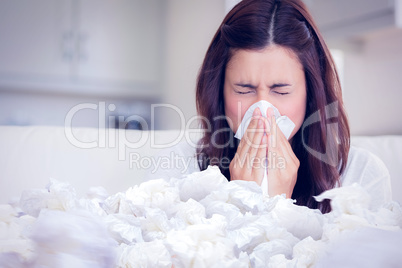 Composite image of brunette sneezing in a tissue