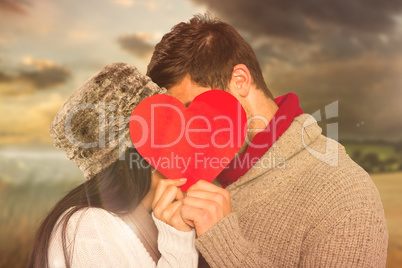 Composite image of young couple kissing behind red heart