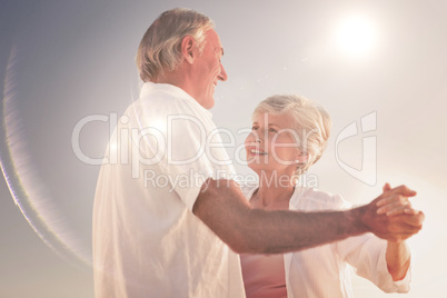 Composite image of senior couple dancing on the beach