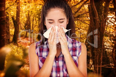 Composite image of beautiful woman sneezing in a tissue