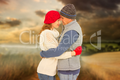 Composite image of happy couple in warm clothing hugging