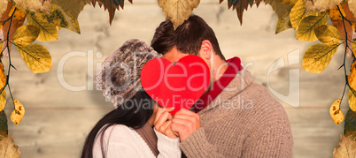 Composite image of young couple kissing behind red heart