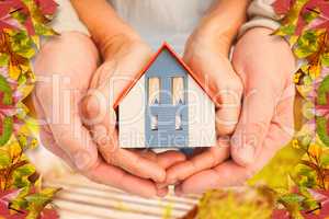 Composite image of couple holding small model house in hands