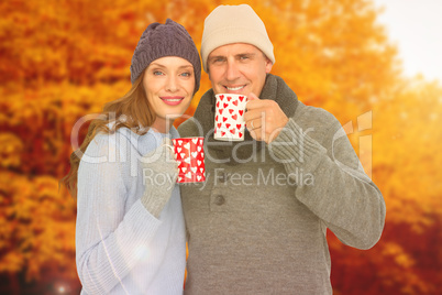 Composite image of happy couple in warm clothing holding mugs