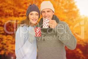 Composite image of happy couple in warm clothing holding mugs