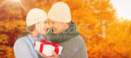 Composite image of casual couple in warm clothing holding gift