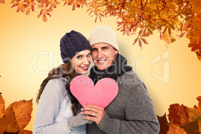 Composite image of happy couple in warm clothing holding heart