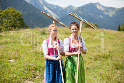 Zwei Bäuerinnen im Dirndl mit Rechen auf einer Almwiese