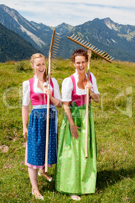 Zwei freudige Frauen im Dirndl mit Rechen haben Spaß bei der Arbeit