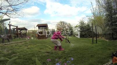 Happy blonde girl watering  in the summer garden