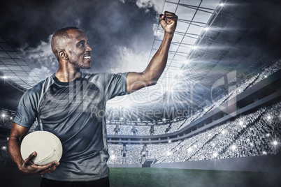 Composite image of sportsman with clenched fist holding rugby ba