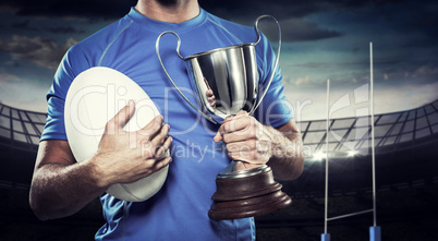 Composite image of rugby player holding trophy and ball