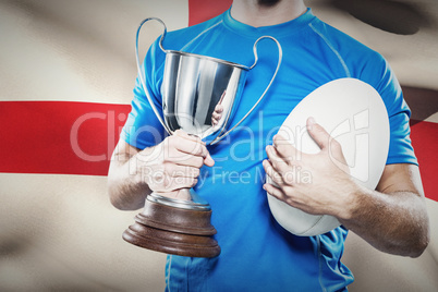 Composite image of rugby player holding trophy and ball