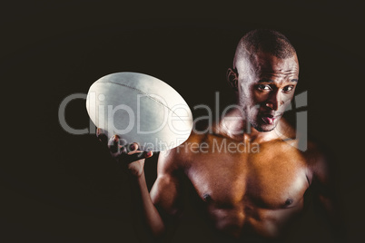 Portrait of confident shirtless sportsman holding rugby ball