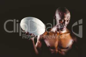 Portrait of confident shirtless sportsman holding rugby ball