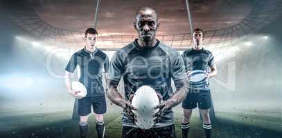 Composite image of serious rugby player in black jersey holding ball