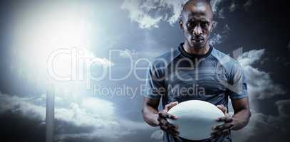 Composite image of portrait of serious sportsman holding rugby b