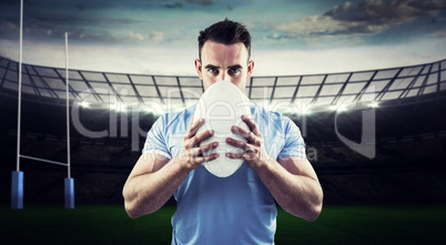 Composite image of rugby player looking at camera with ball