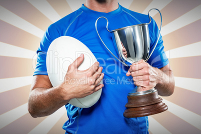 Composite image of rugby player holding trophy and ball